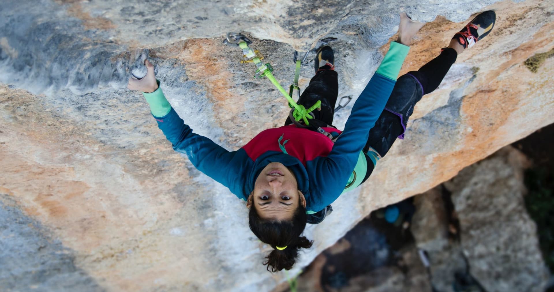 Person looking upwards as they are climbing a steep rock