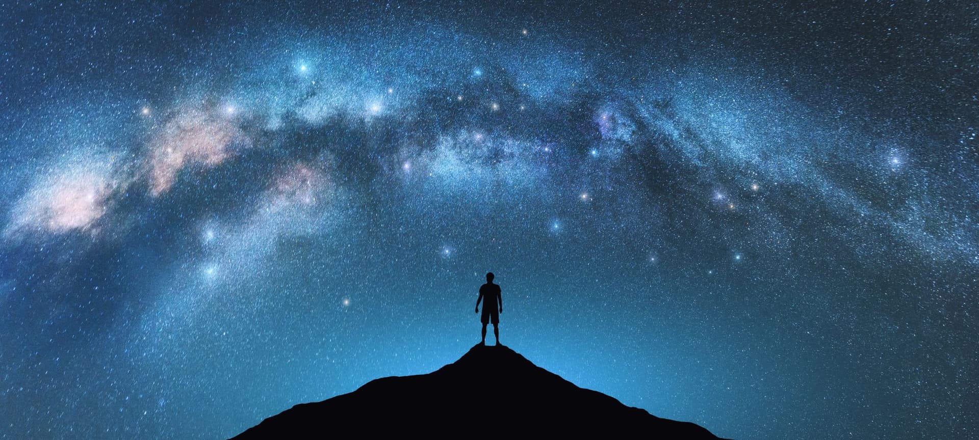 silhouette of a person standing on a mountain peak surrounded by a background of space/night sky