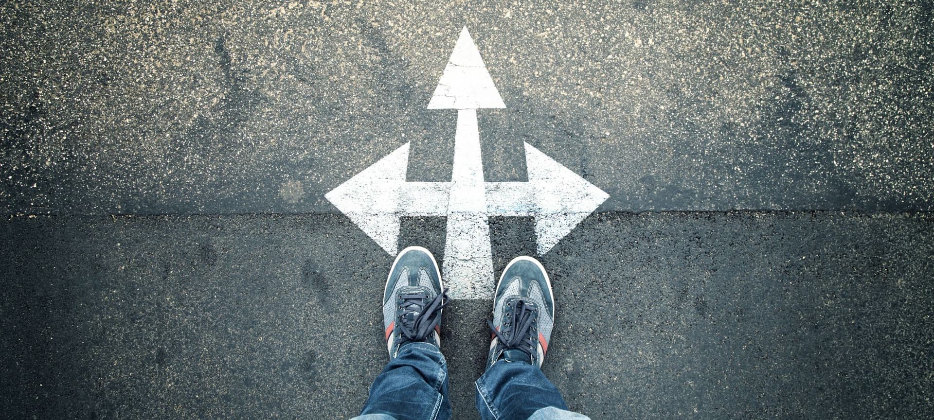 Closeup of person's feet as they stand on pavement with white arrows pointing left, right, and upward