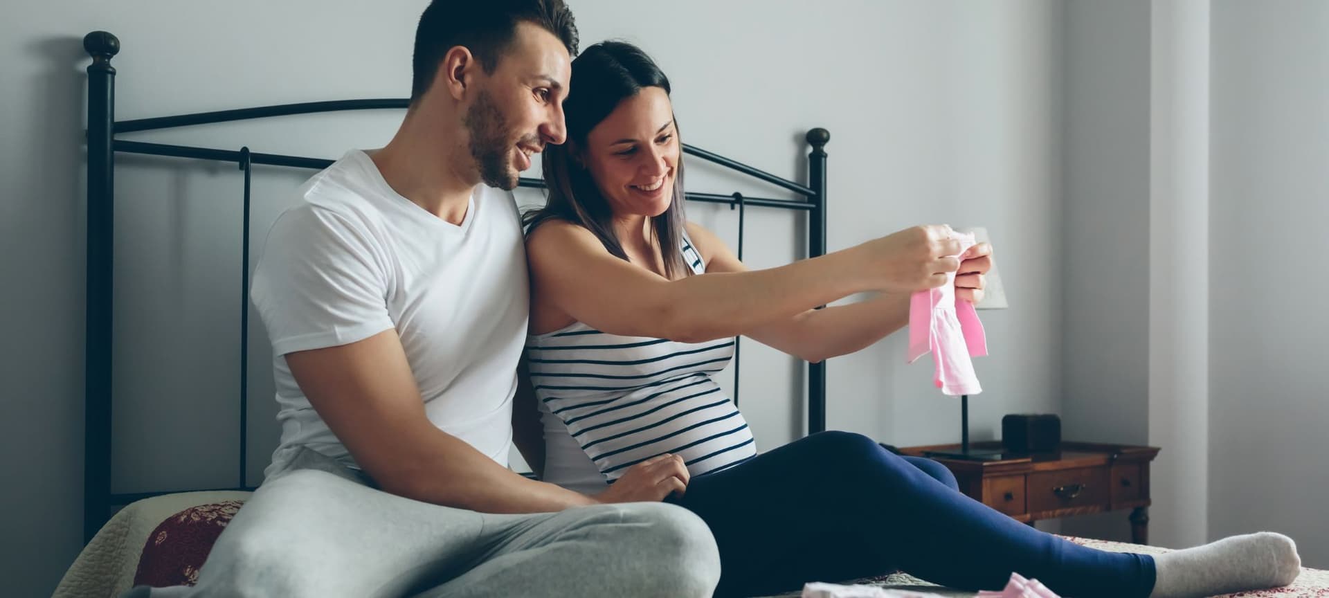 Expecting couple sitting together and lovingly reflecting on arrival of baby as they admire baby clothes