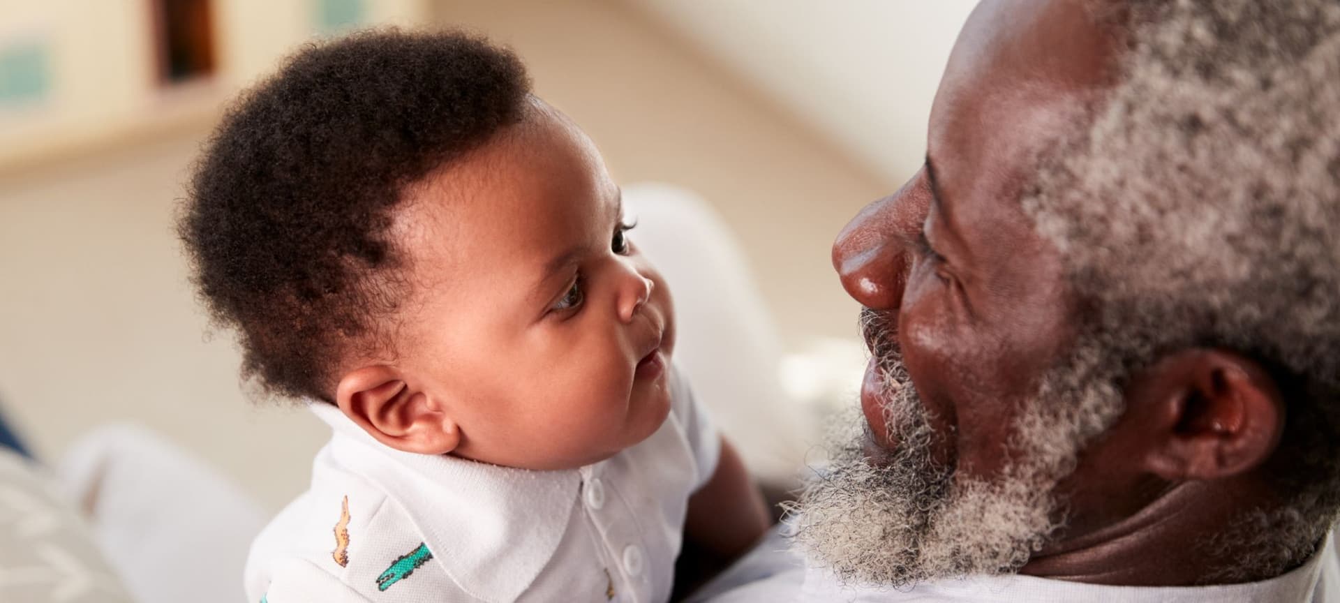 A baby and grandfather look into eachother's eyes. the grandfather smiles