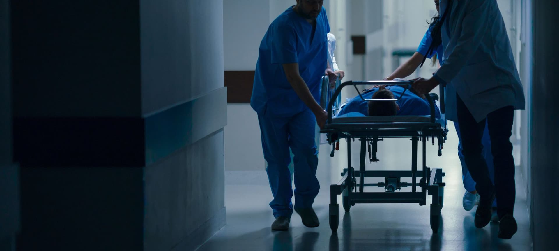 Two doctors pushing a hospital gurney with a patient in a dark hallway