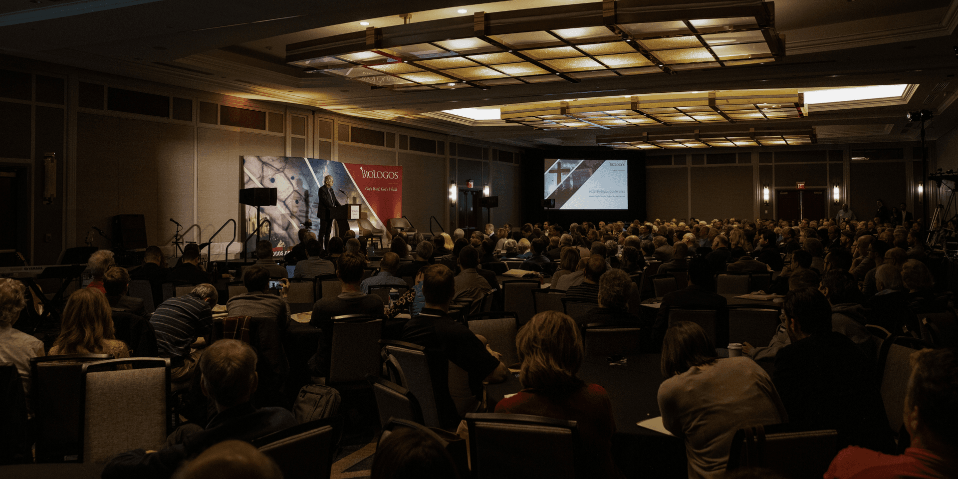A crowd of BioLogos event attendees listens to Francis Collins, who stands at a podium.