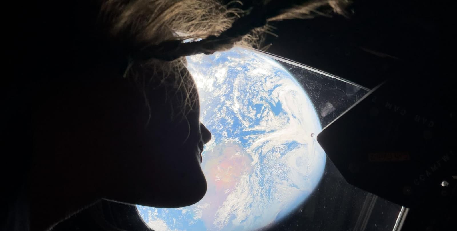 Christina Koch looks out the window of Orion at Earth in the distance.